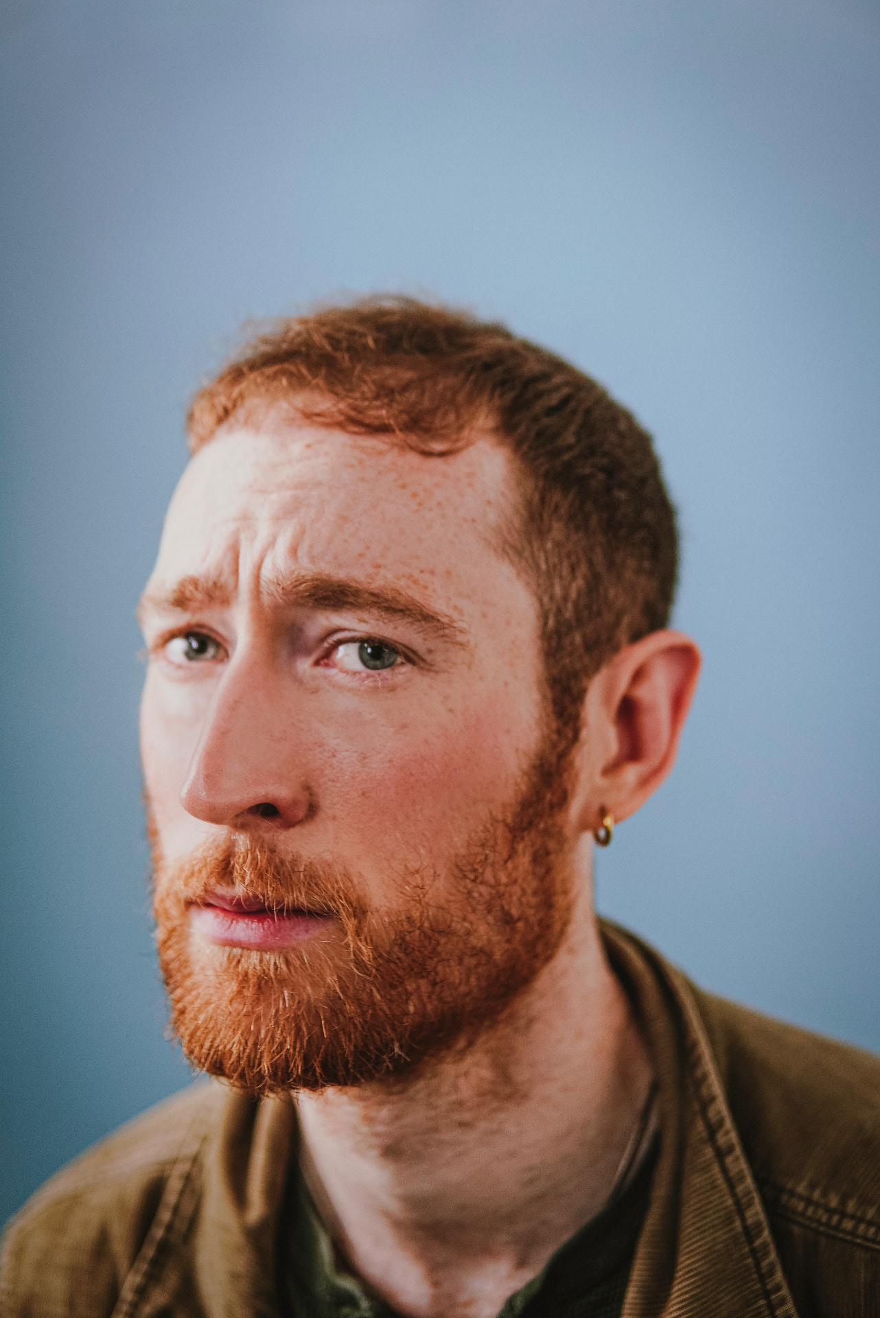 Close-up portrait of a red-haired man with a beard against a blue backdrop