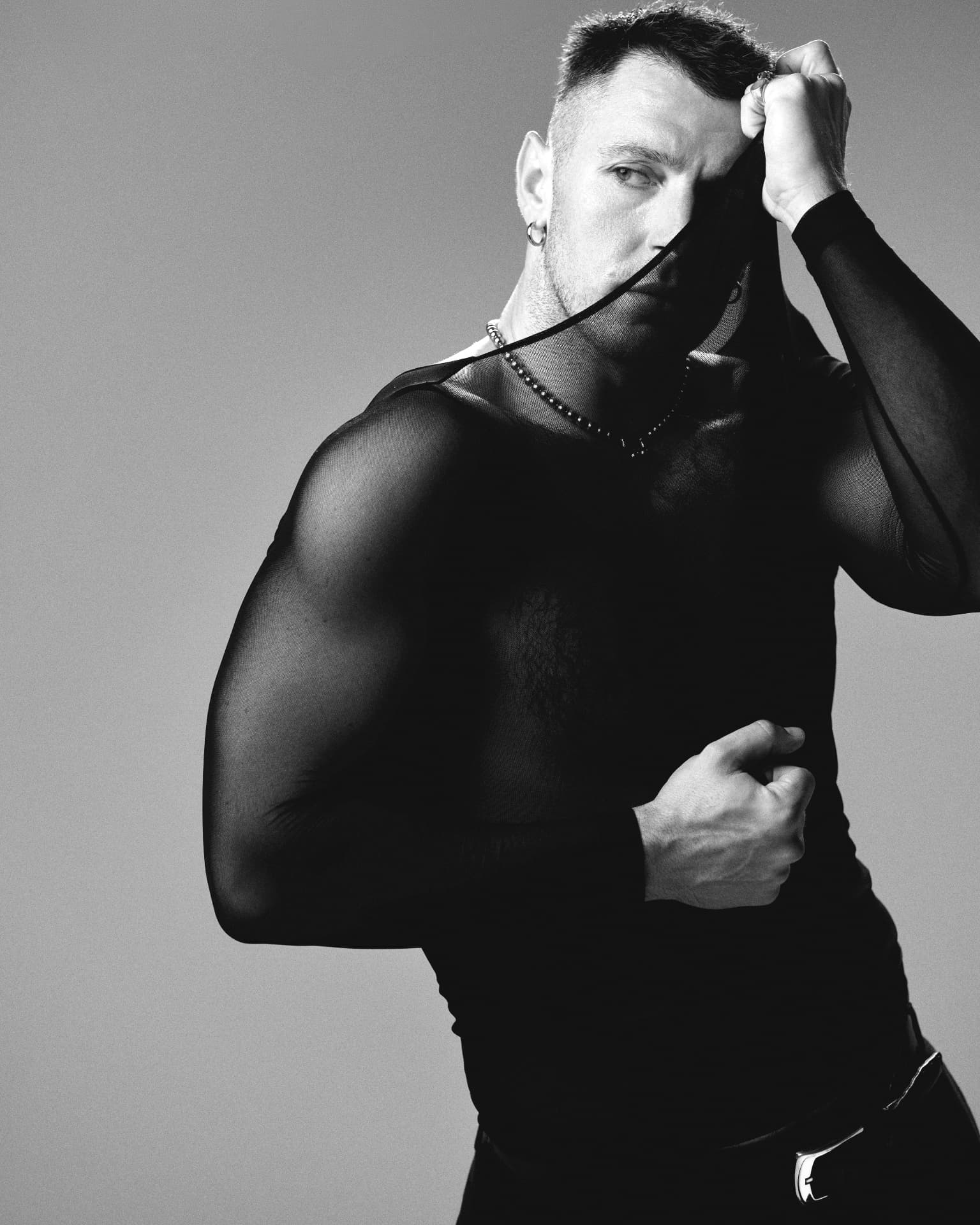 Black-and-white portrait of a man pulling a sheer black top across his face
