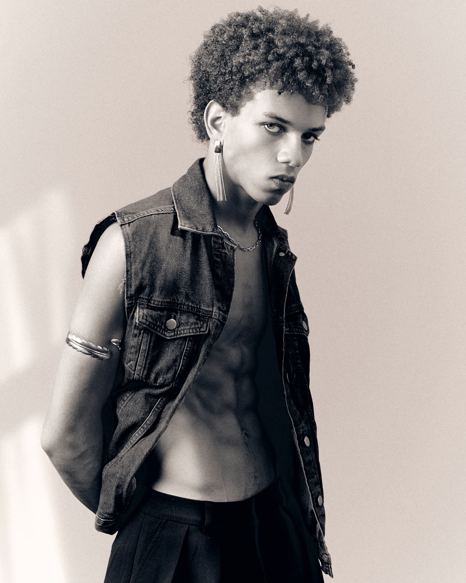 Black-and-white portrait of a man in a sleeveless denim vest, one hand behind his back
