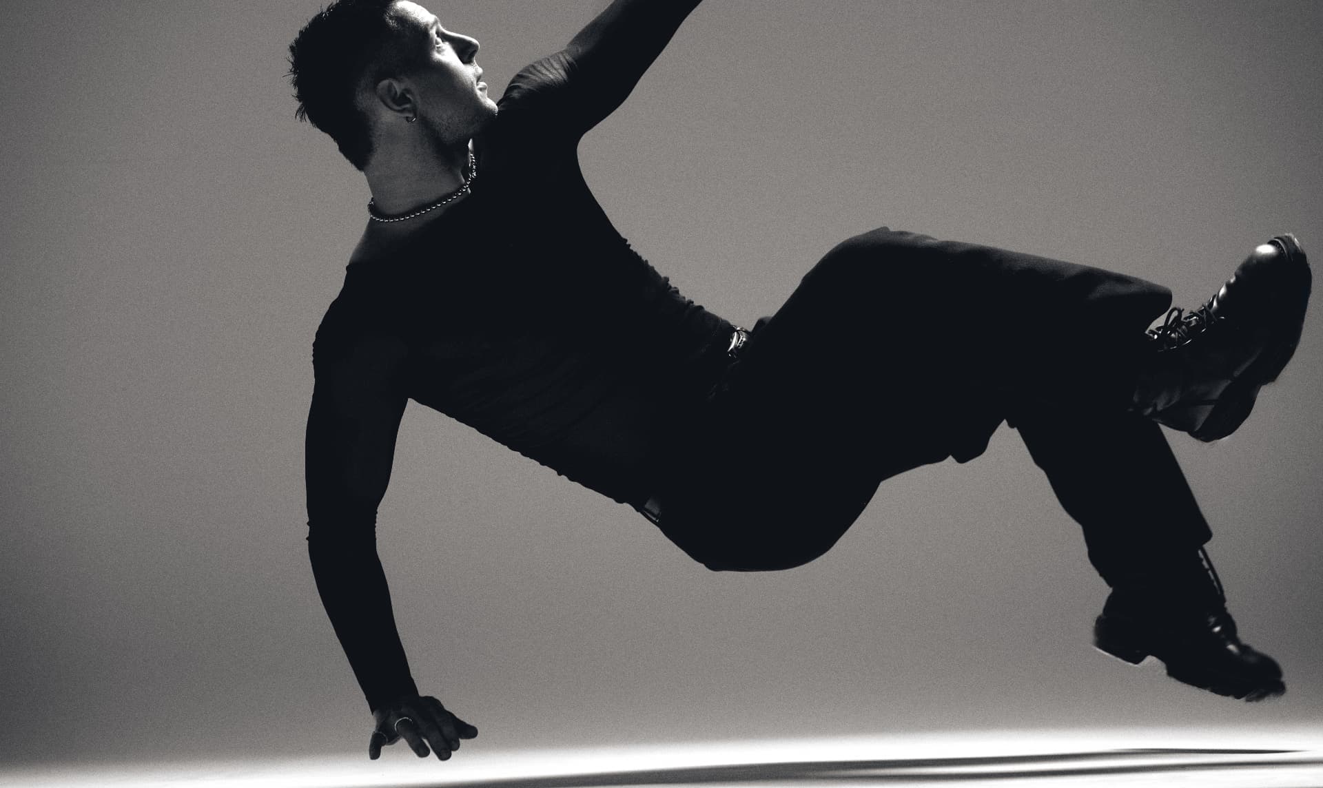 Black-and-white wide shot of a man in black suspended mid-air in a horizontal leap