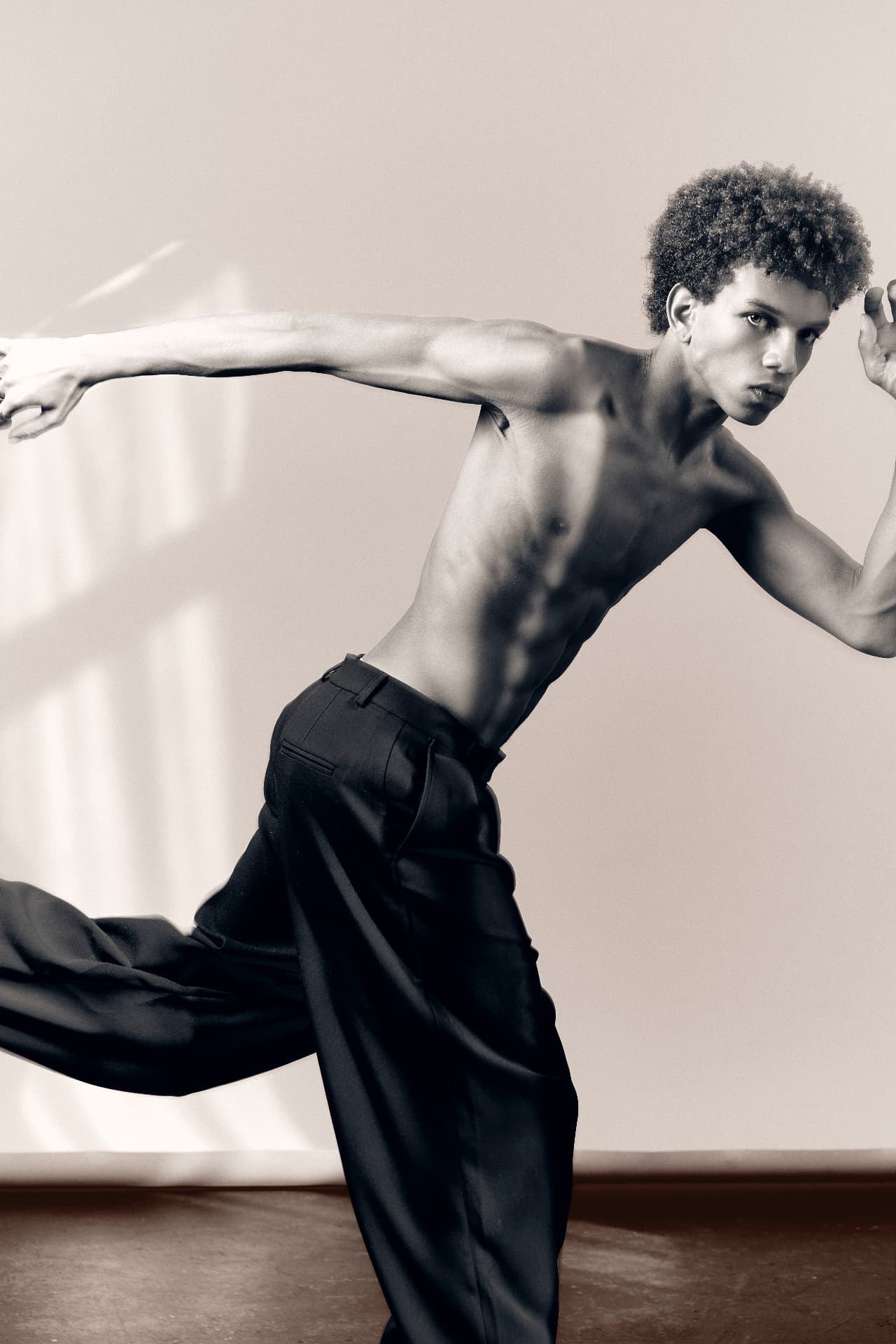 Black-and-white portrait of a shirtless man lunging with one arm outstretched