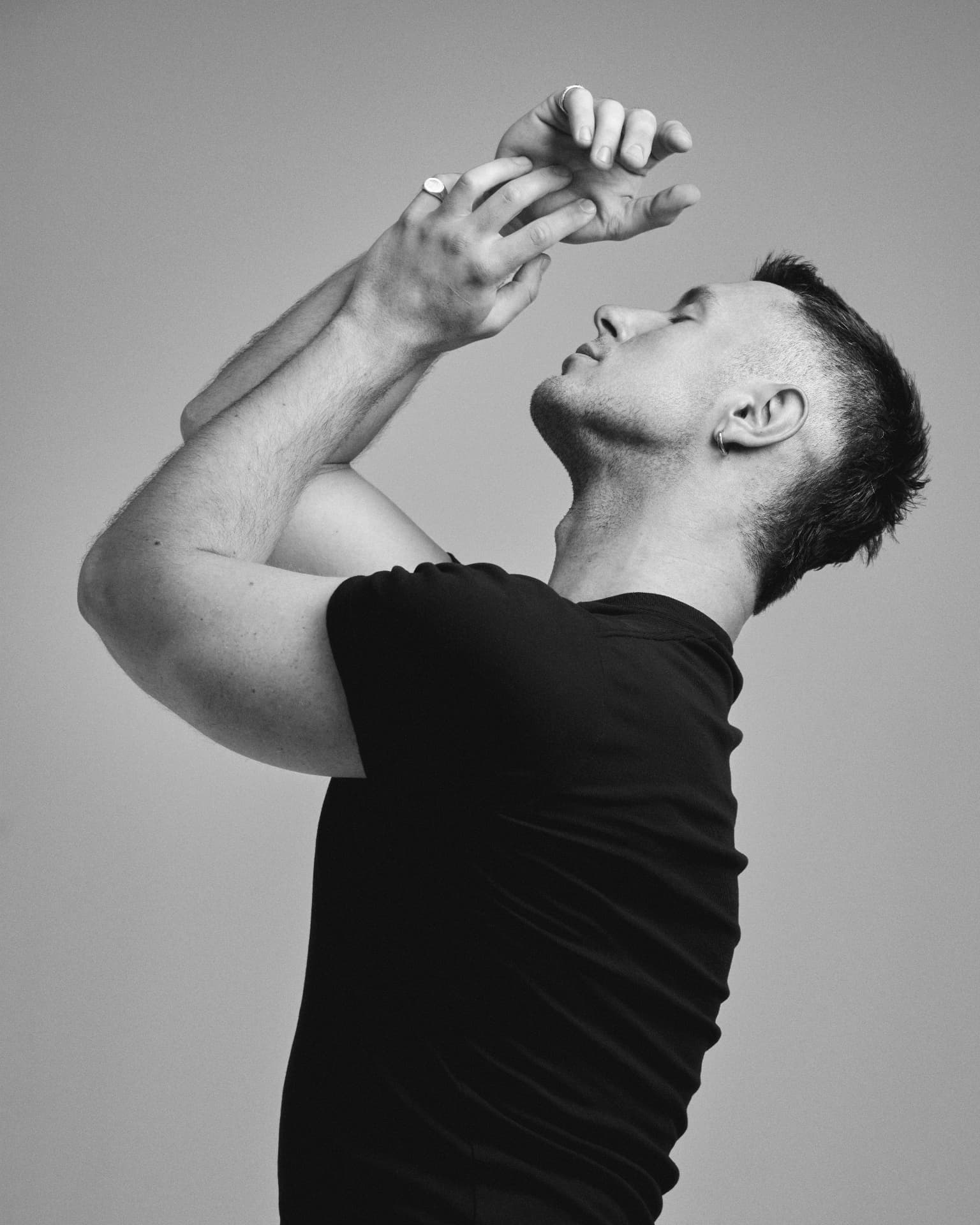 Black-and-white portrait of a man in a black t-shirt arching his neck back, hands raised