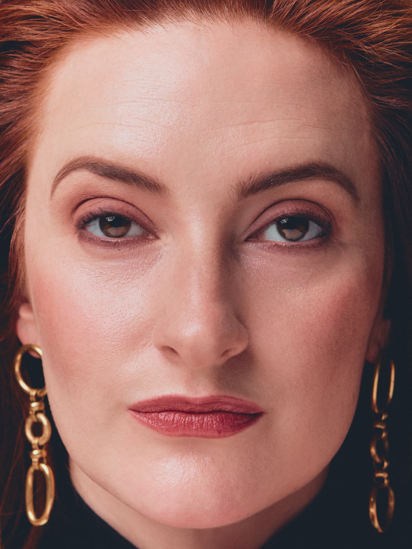 Close-up portrait of a red-haired woman wearing gold chain earrings