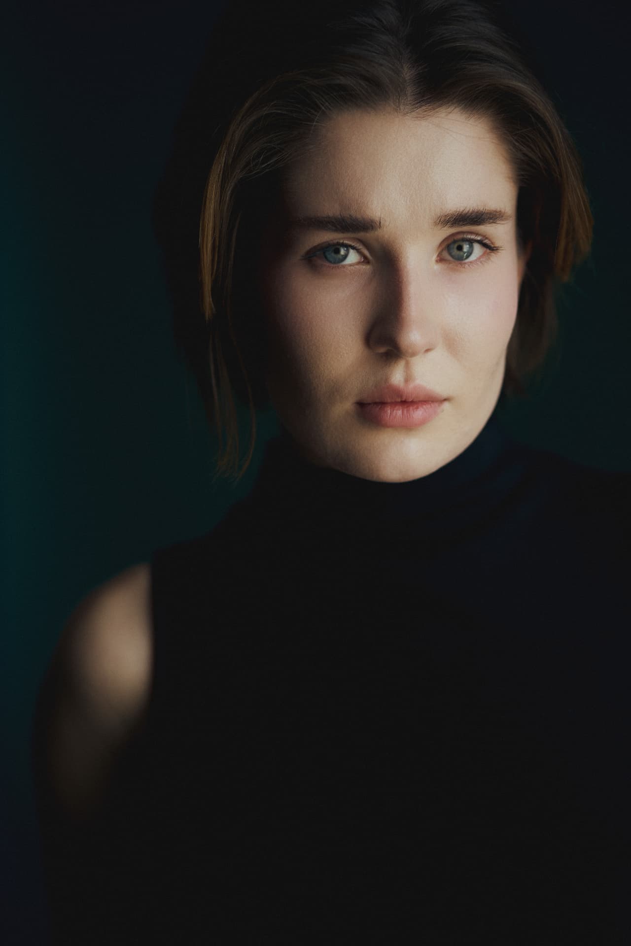 Moody close-up portrait of a woman with short hair in a black turtleneck against a dark background