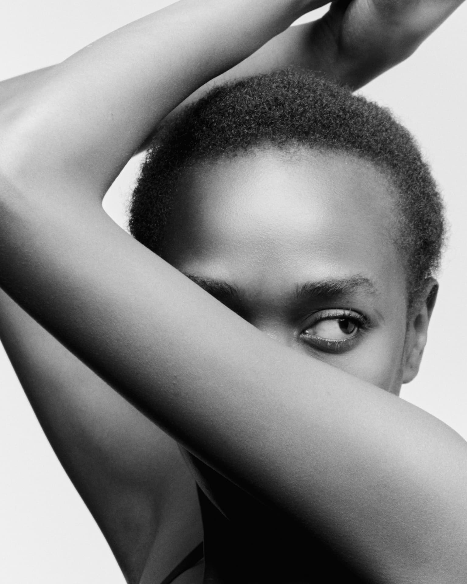 Black-and-white close-up portrait of a woman with short hair, arms framing her face