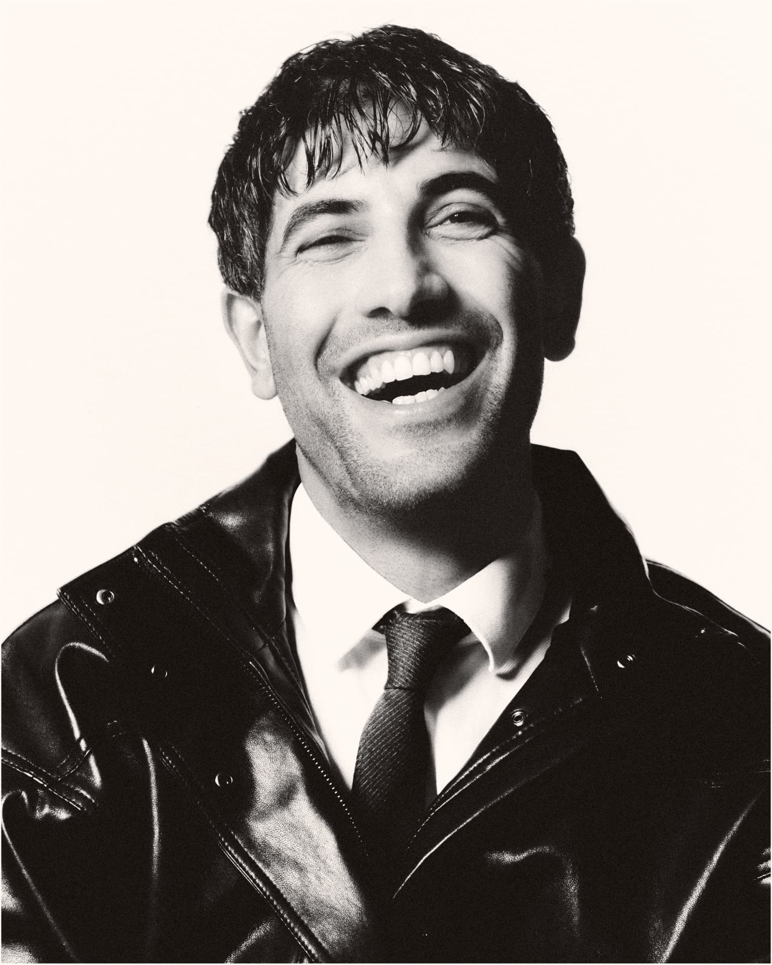 Black-and-white portrait of a laughing man in a leather jacket and tie