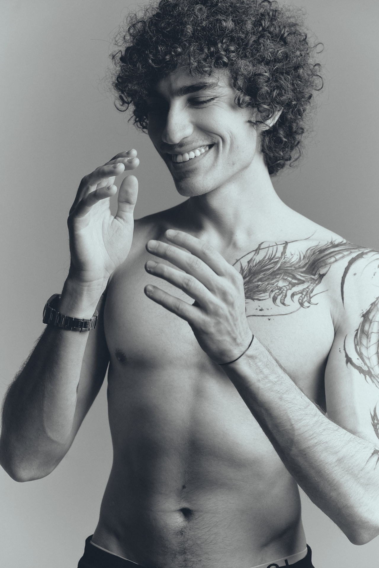 Black-and-white portrait of a smiling shirtless man with a tattooed arm