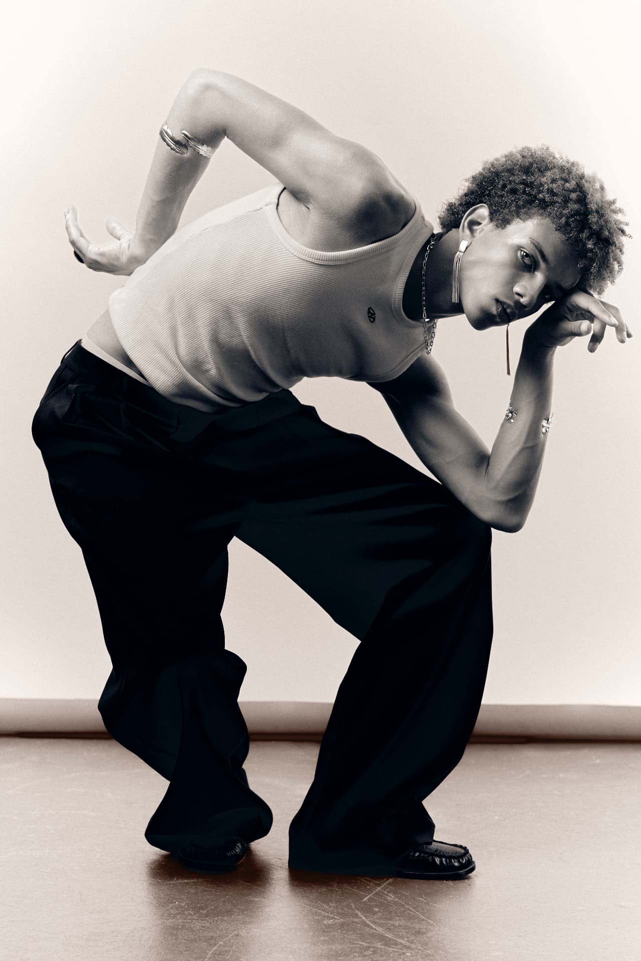 Black-and-white full-length portrait of a man crouching in a tank top and wide trousers