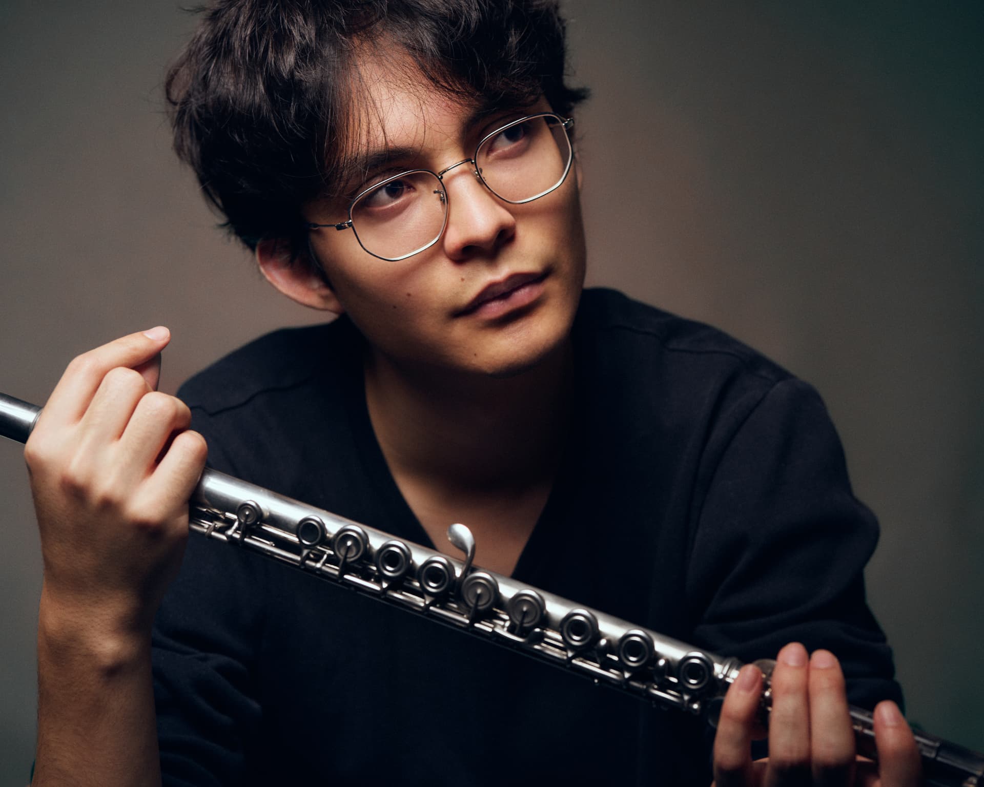 Close-up portrait of a young man in glasses resting a flute on his shoulder