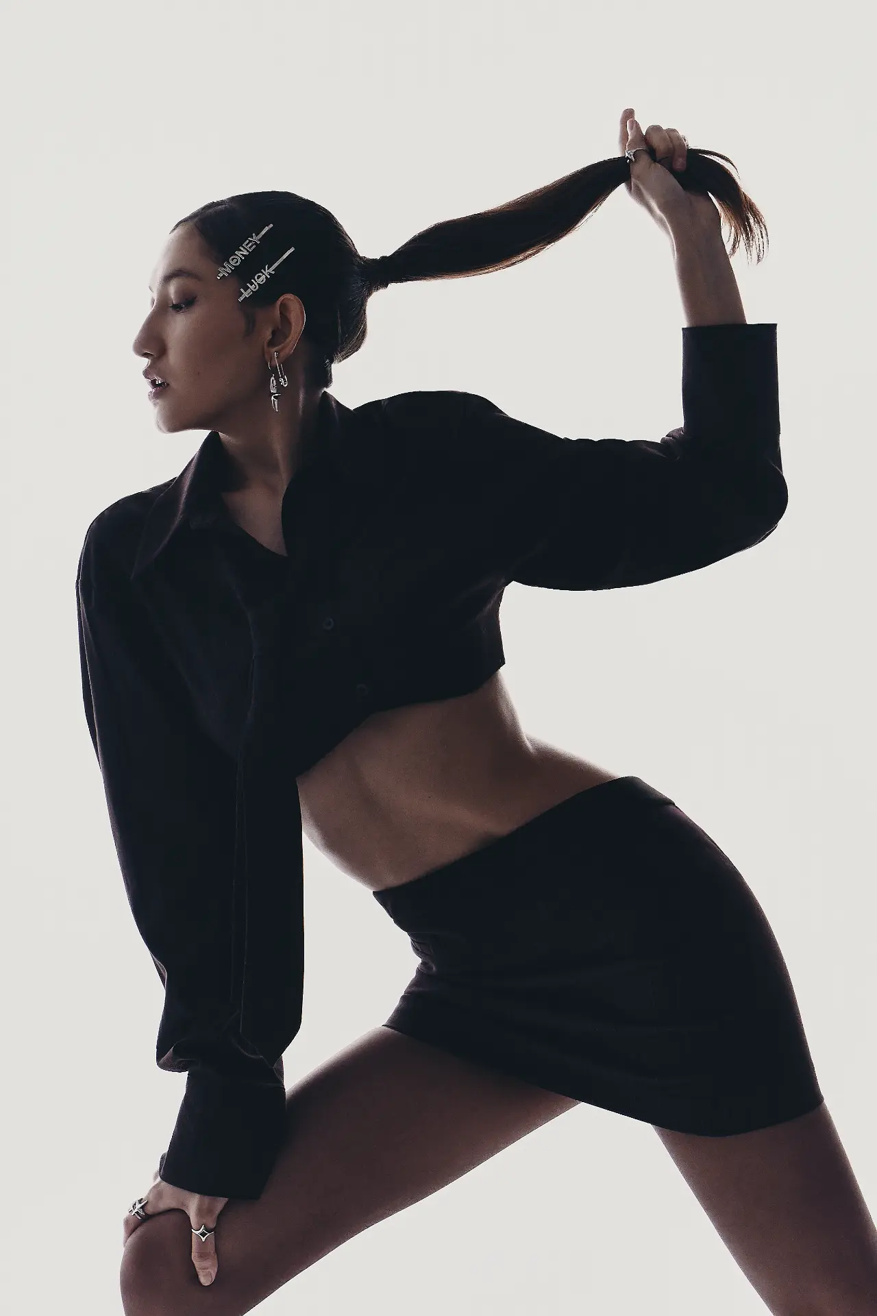 Full-length portrait of a woman in a black cropped shirt and mini skirt pulling her ponytail