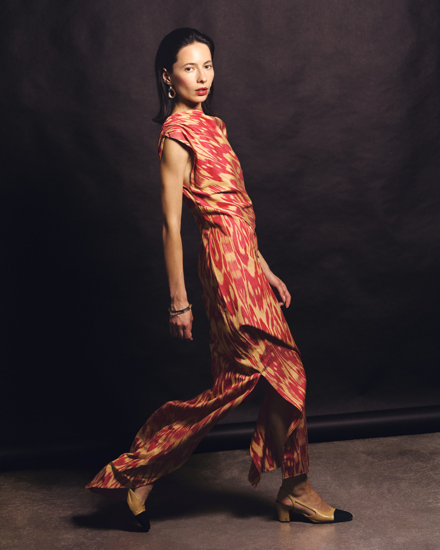 Full-length portrait of a woman in a red and gold patterned outfit on a dark set