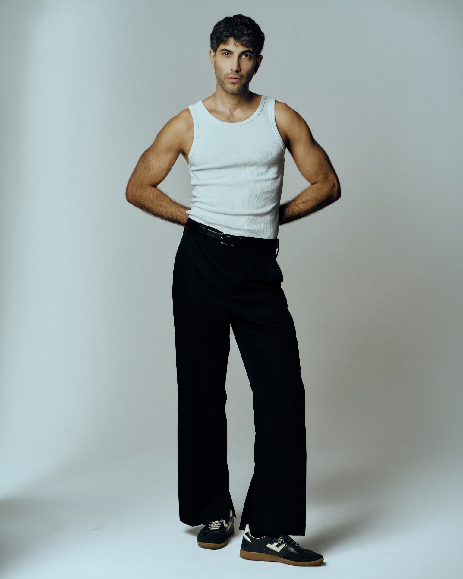Full-length studio portrait of a man in a white tank top and black trousers
