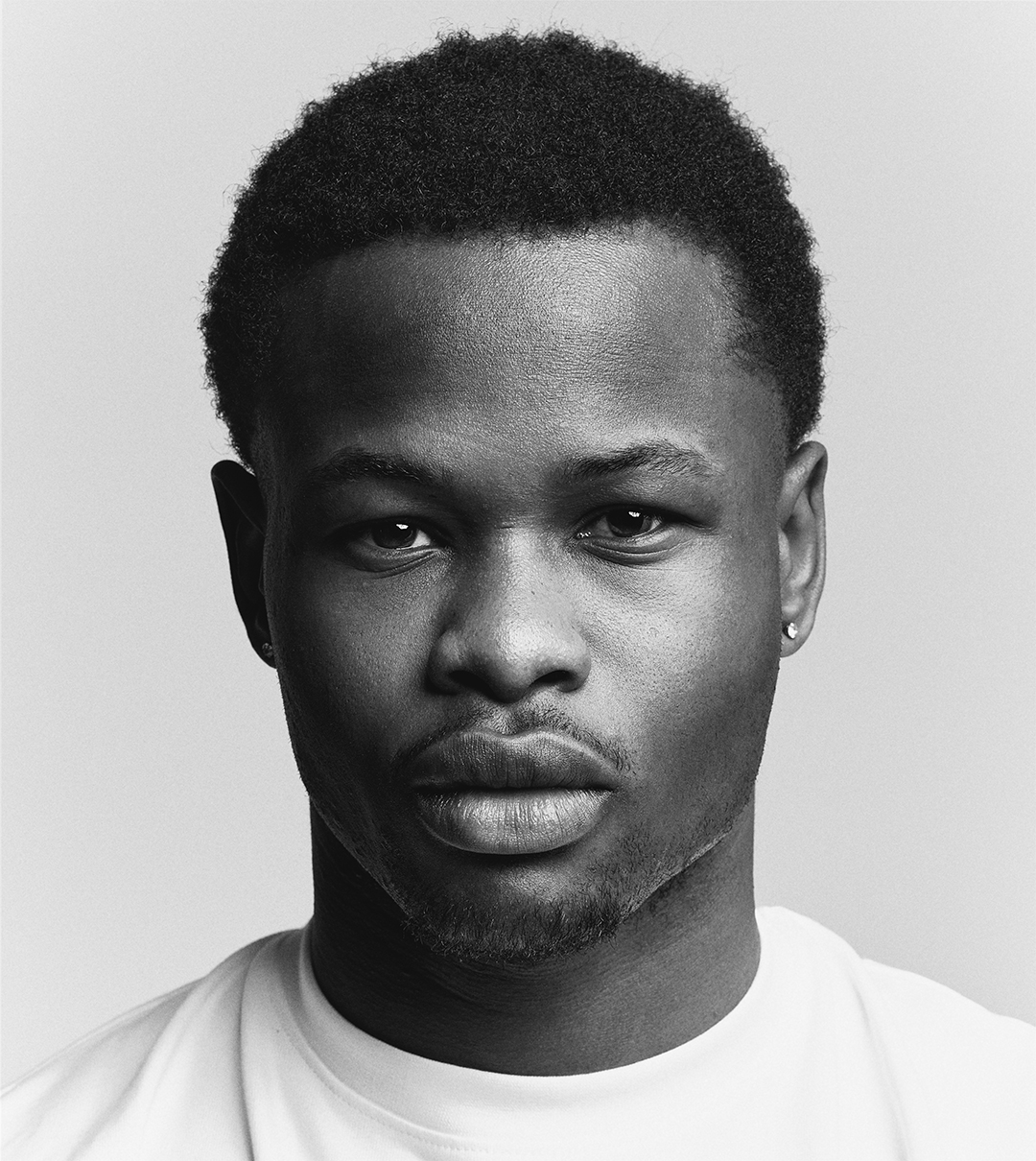 Black-and-white close-up portrait of a young man in a white t-shirt against a grey background