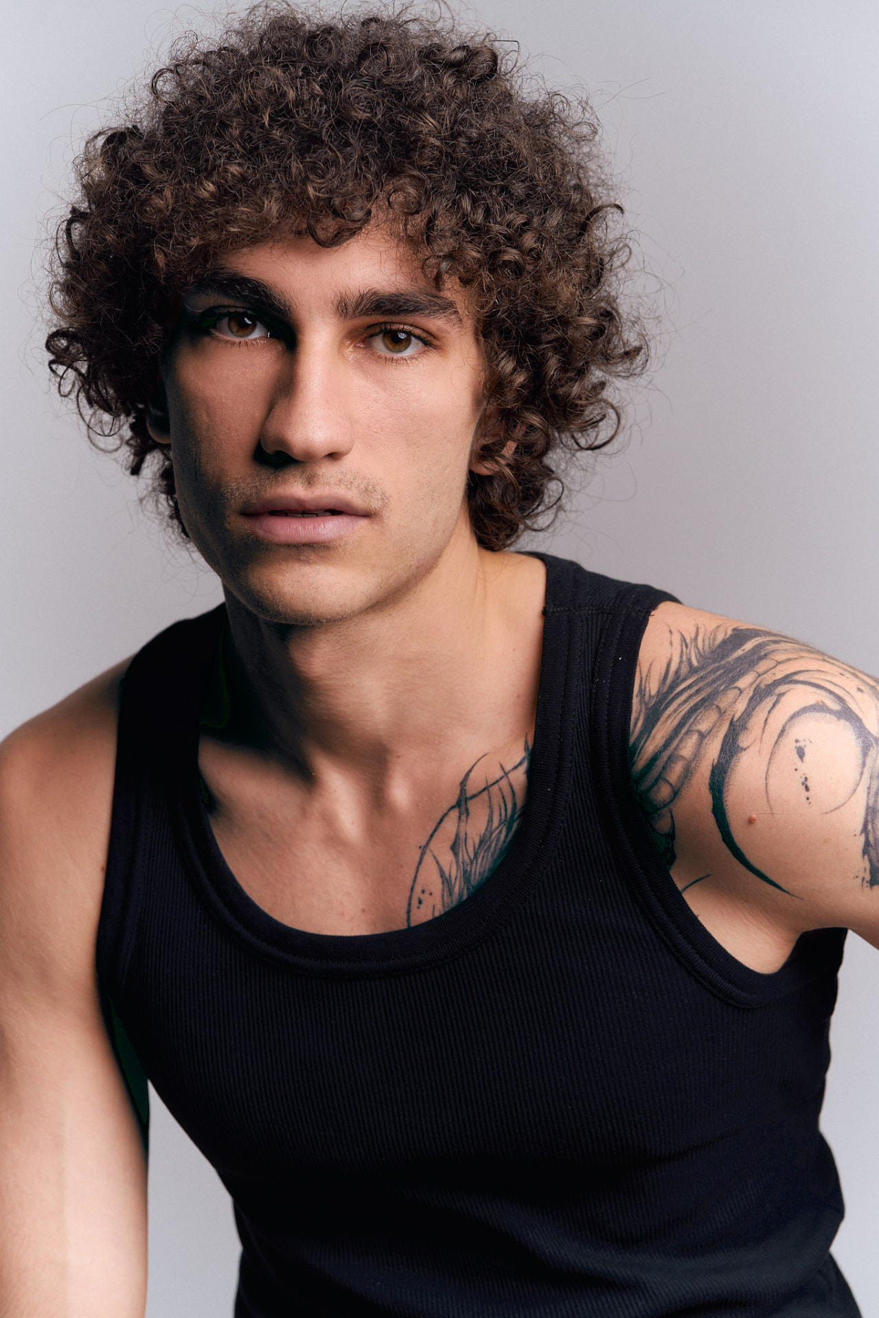 Portrait of a curly-haired man with tattoos wearing a black tank top